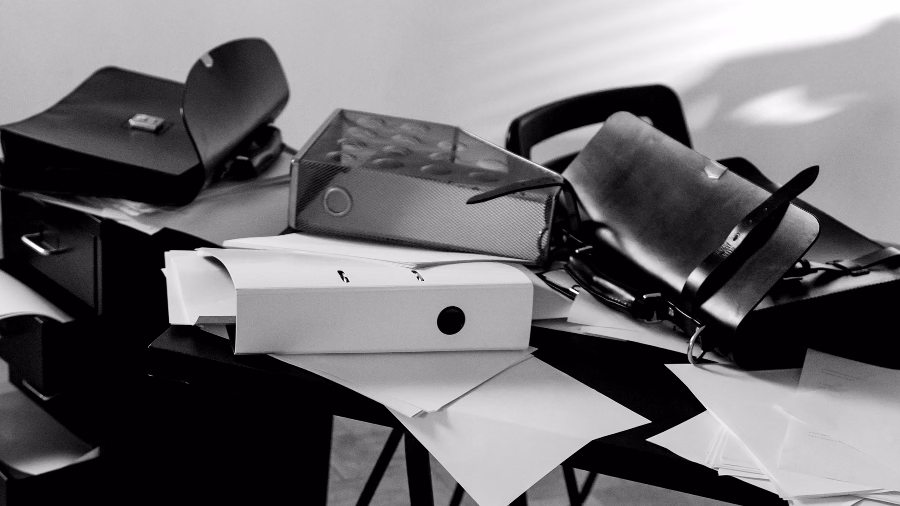 A desk covered in binders and scattered paper, in black and white
