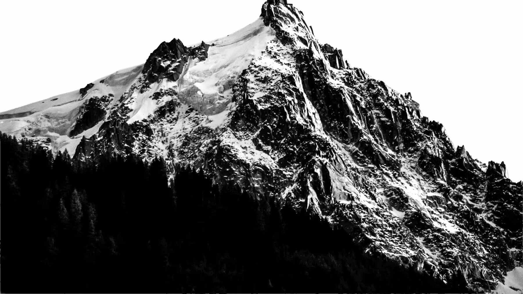 Sommet enneigé et arête rocheuse au-dessus d'une forêt, en noir et blanc
