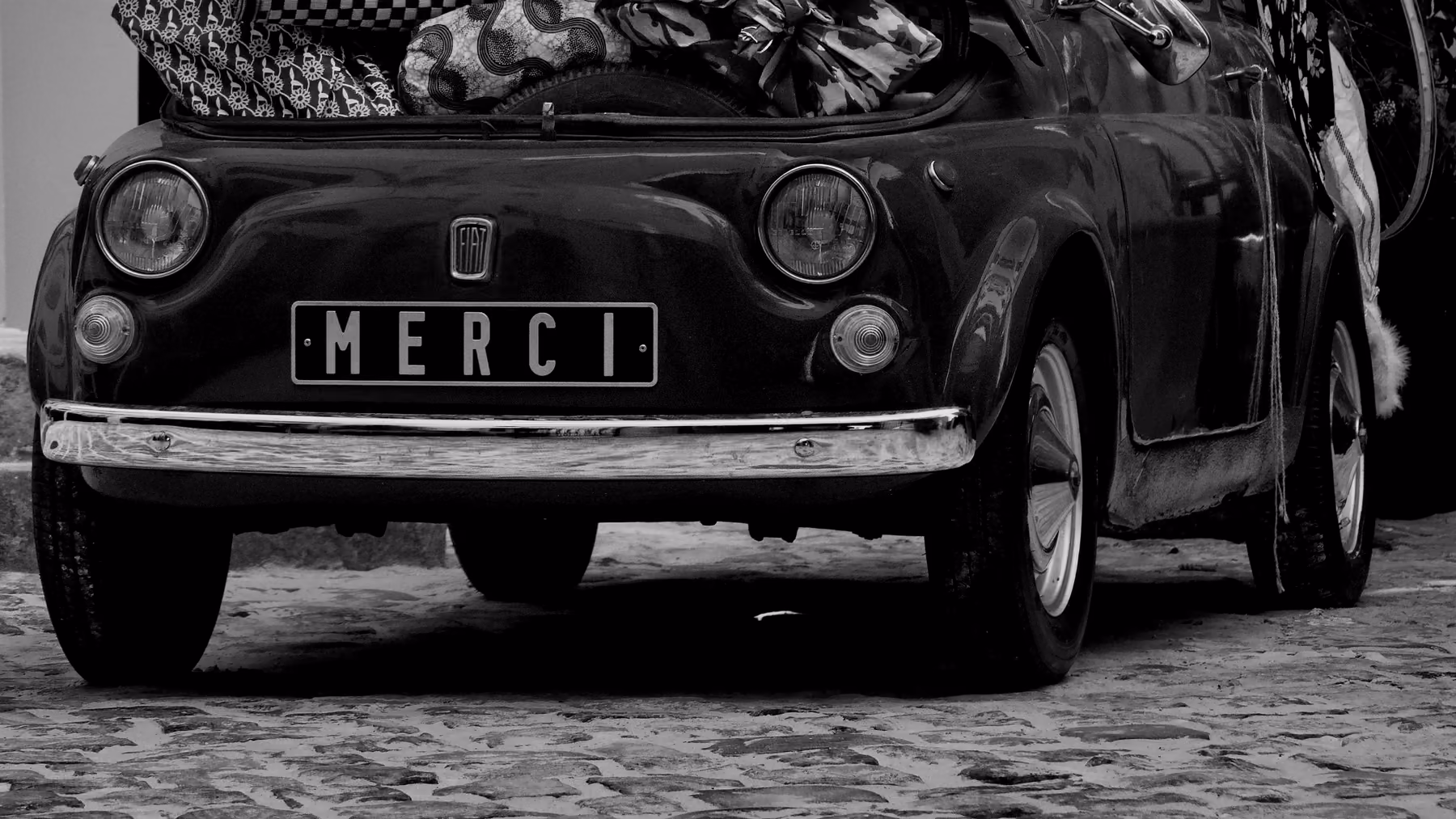 A small vintage car loaded with luggage up to the roof, in black and white