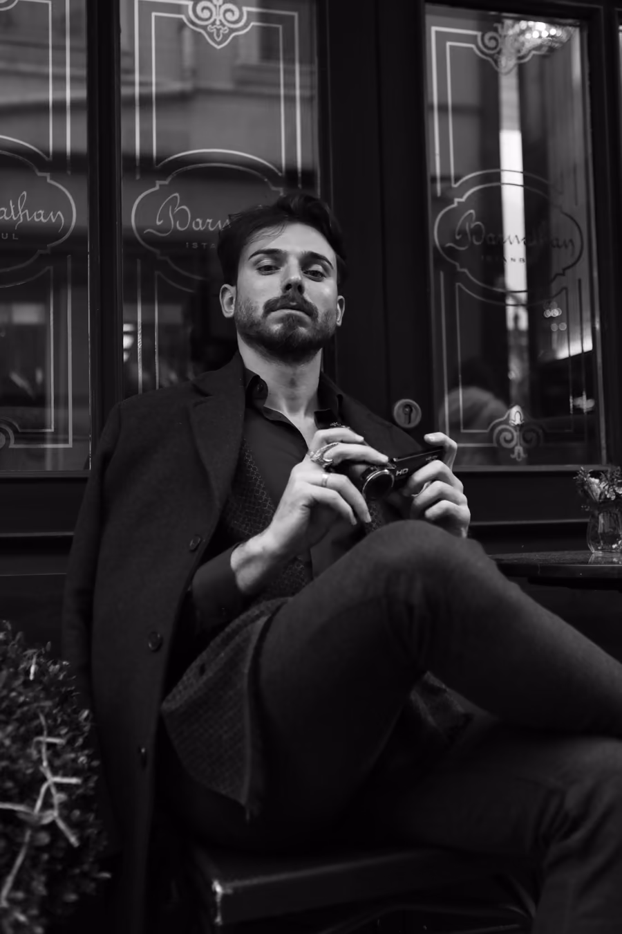 Ein Mann sitzt auf einer Caféterrasse, Kamera in der Hand, in Schwarz-Weiß