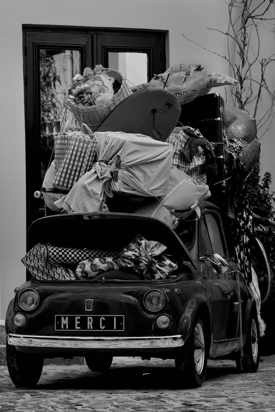 A small vintage car loaded with luggage up to the roof, in black and white